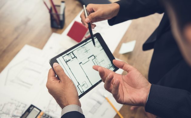 Real estate agent with client or architect team checking a housing model and its blueprints digitally using a tablet Real estate agent with client or architect team discussing a housing model and its blueprints digitally using a tablet computer